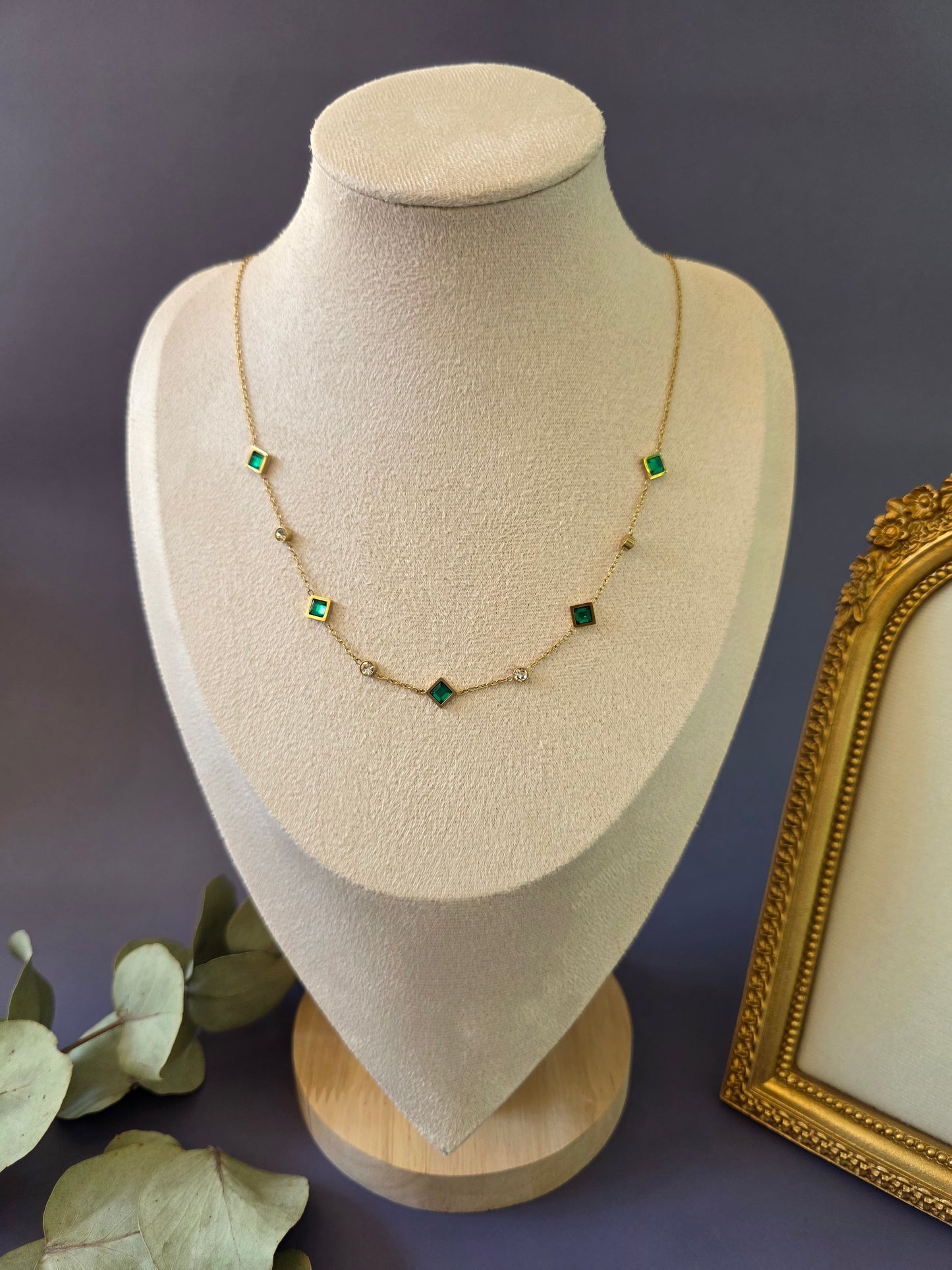Emerald Glow Station necklace with vibrant green stones displayed on a jewelry bust. A tarnish-proof gold-plated station-style necklace designed for a sophisticated and radiant look - My Silver Lining.