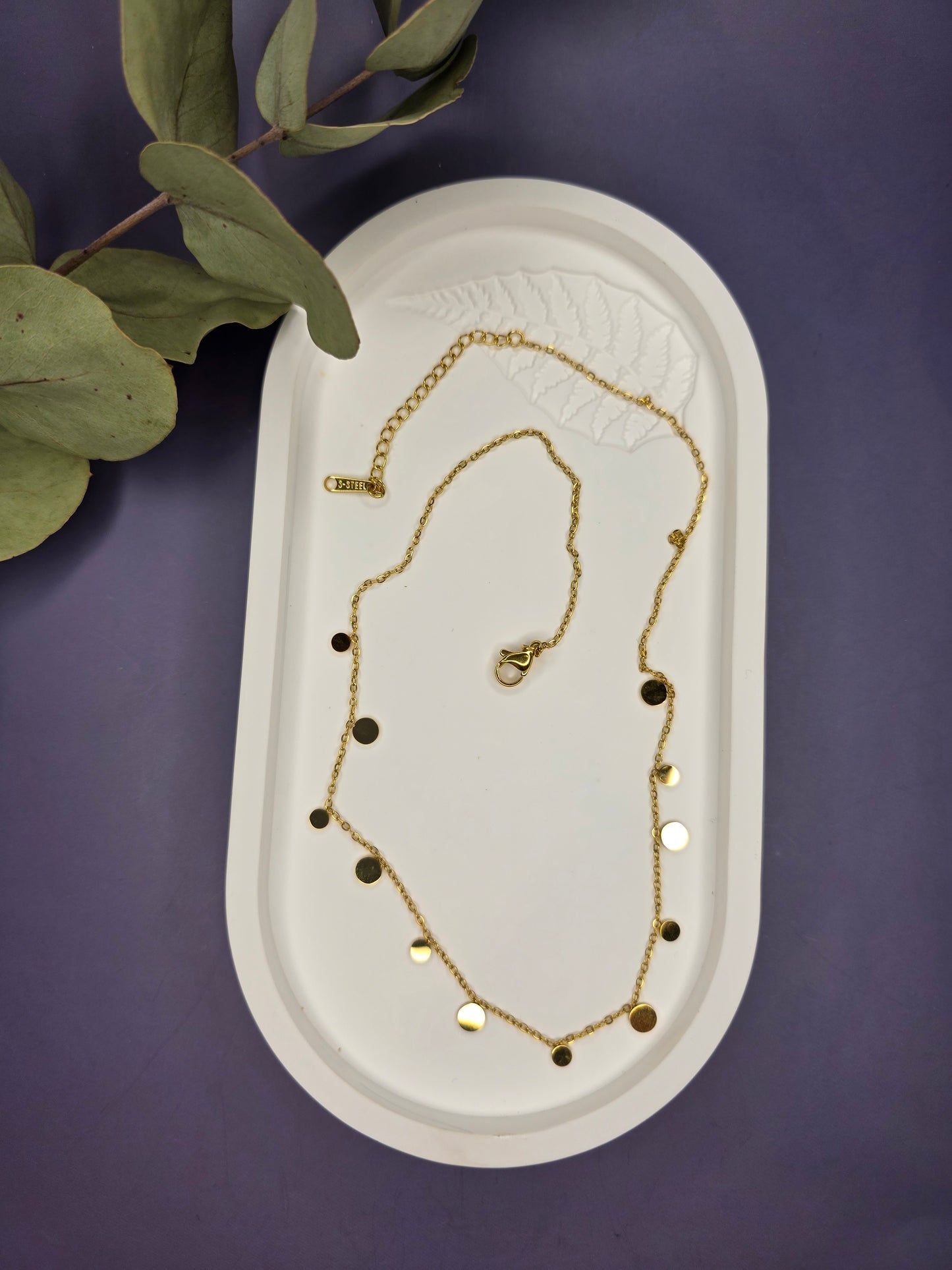 Golden Dewdrop necklace nestled in a white oval stone tray. This tarnish-resistant 304 stainless steel necklace showcases its delicate dangle disc design and luxury gold tone - My Silver Lining.