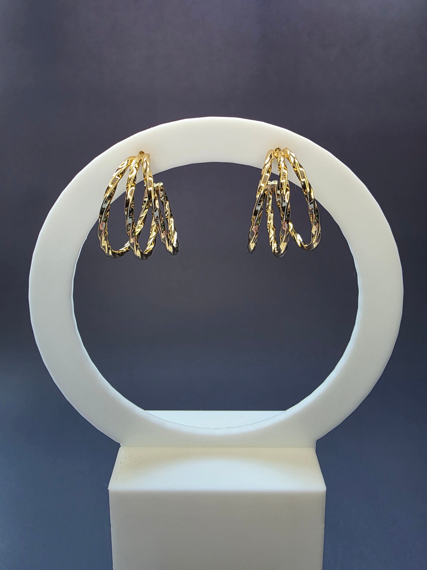 Golden Twist hoops suspended from a golden white arch jewelry stand. These 2.5cm 304 stainless steel earrings showcase an intricate twisted triple-layer design and a high-polish gold tone - My Silver Lining.