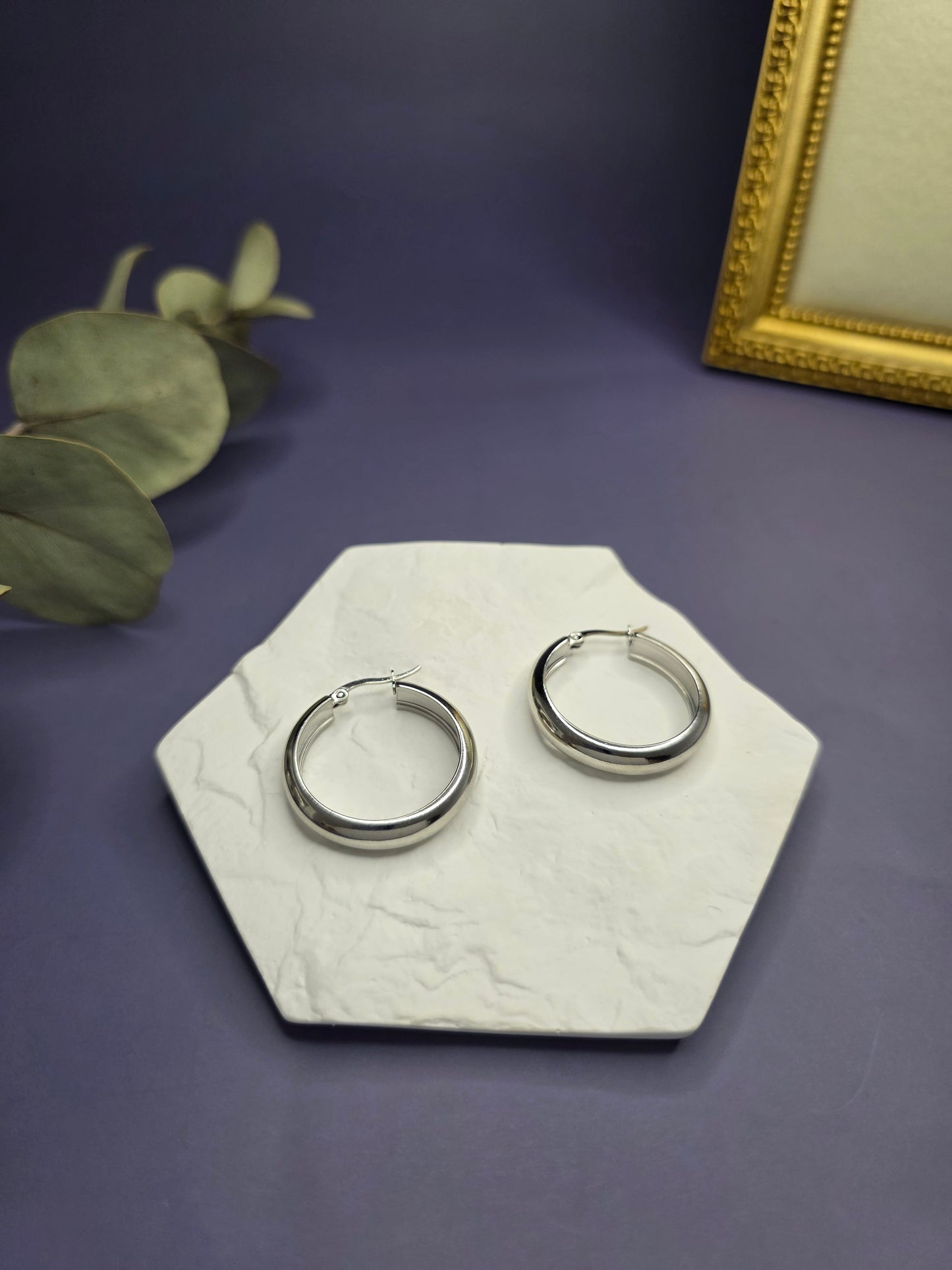 Optimized silver halo hoops displayed on a white textured hexagon stone. These 3cm waterproof 304 stainless steel earrings offer a polished, tarnish-resistant finish for modern every day elegance - My Silver Lining.