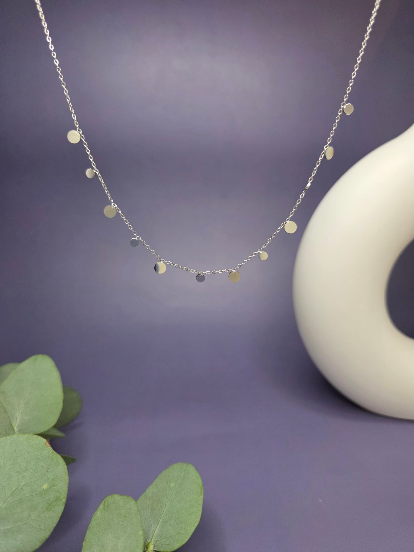 Close-up of a Silver Dewdrop Necklace with circular charms on a stainless steel chain, displayed against a purple background for My Silver Lining.