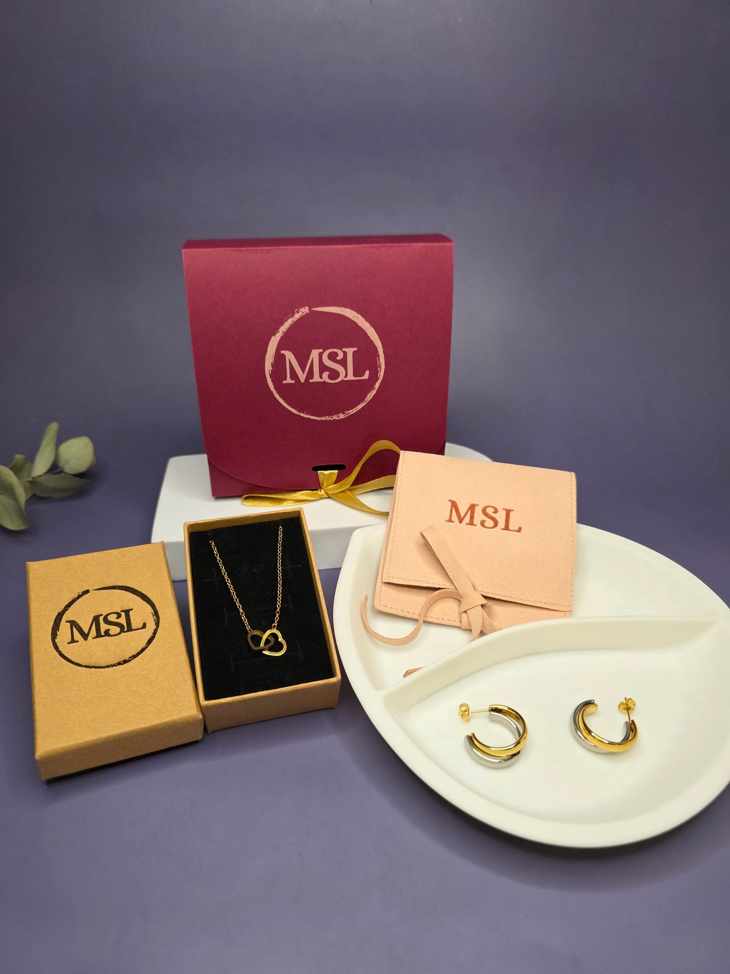 A luxury Valentine’s gift box for her featuring a gold interlocking heart necklace and Gemini mixed-metal hoop earrings on a white display tray, optimized for romantic gifting.
