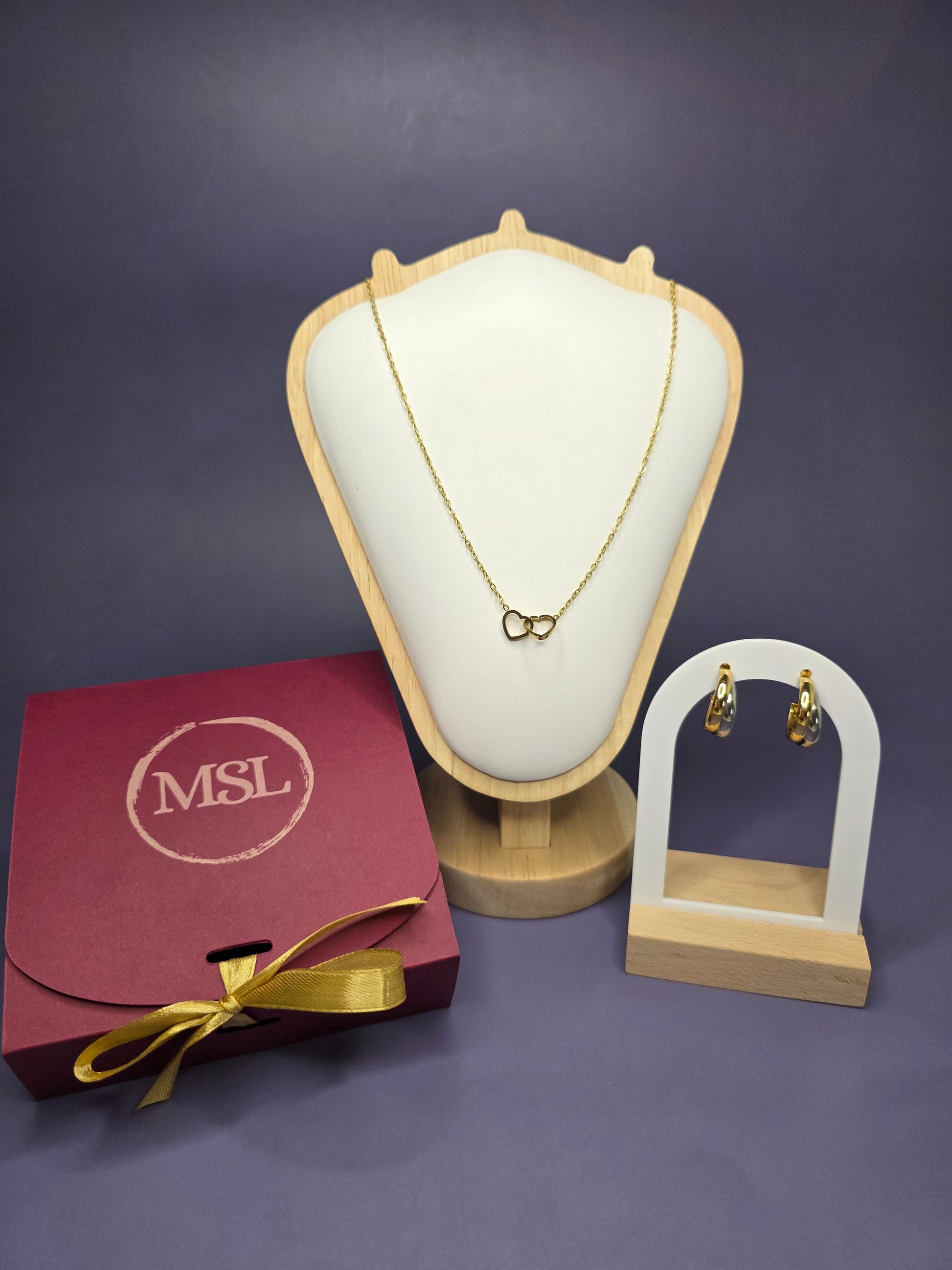 A luxury Valentine’s gift box for her featuring a gold interlocking heart necklace and Gemini mixed-metal hoop earrings on a white display tray, optimized for romantic gifting.