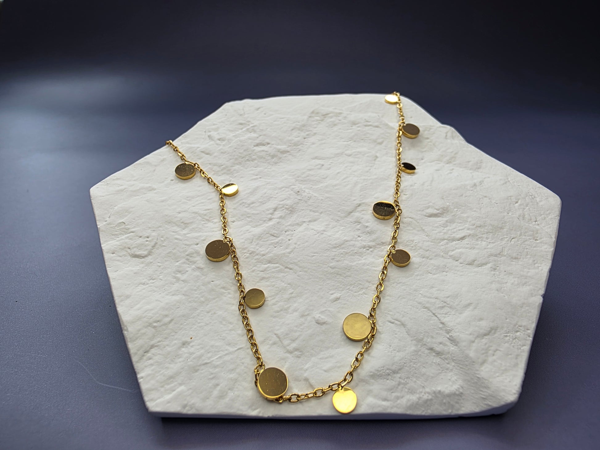 Delicate gold-toned necklace featuring multiple small, flat, dangling disc or coin pendants evenly spaced along the chain, perfect for layering.