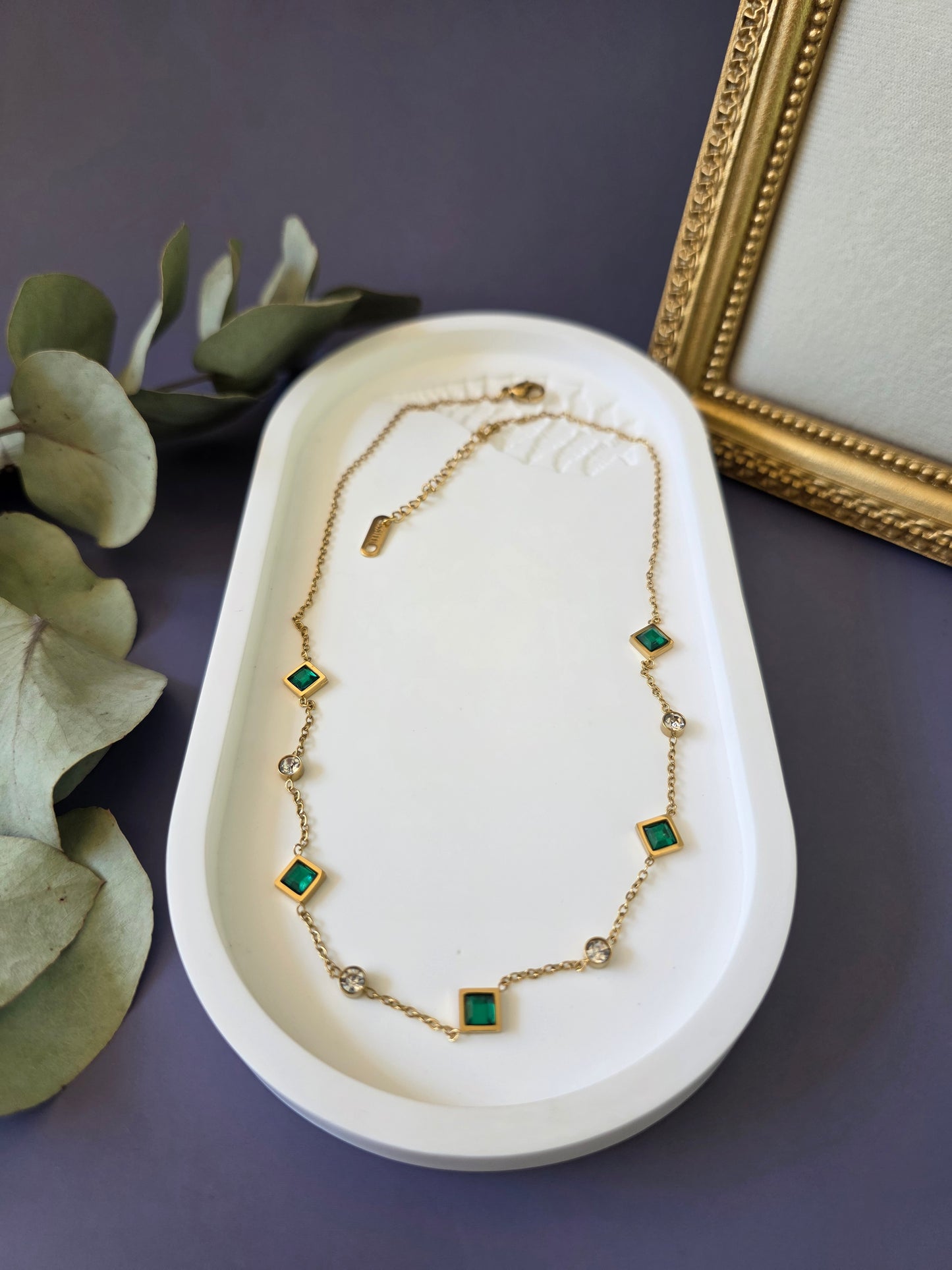 Flatlay of the Emerald Glow gold station necklace on a white oval jewelry tray. High-quality hypoallergenic stainless steel necklace with green cubic zirconia and clear crystal accents - My Silver Lining.