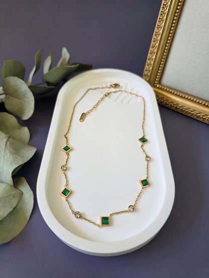 Flatlay of the Emerald Glow gold station necklace on a white oval jewelry tray. High-quality hypoallergenic stainless steel necklace with green cubic zirconia and clear crystal accents - My Silver Lining.