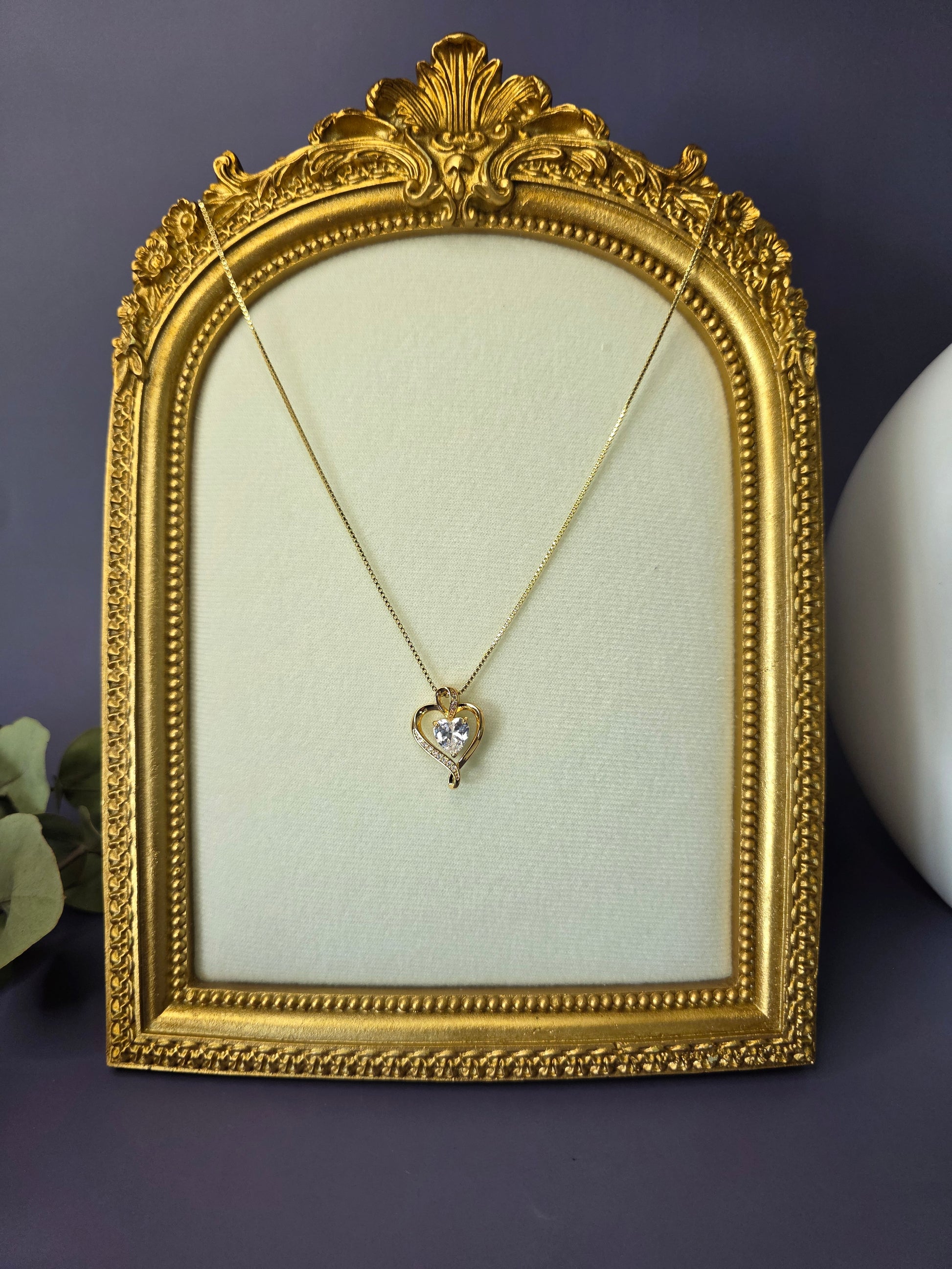 The Eternal Heart Solitaire necklace displayed in a vintage gold frame. A timeless 18K gold heart pendant symbolizing enduring love and commitment with a graceful sparkle - My Silver Lining.