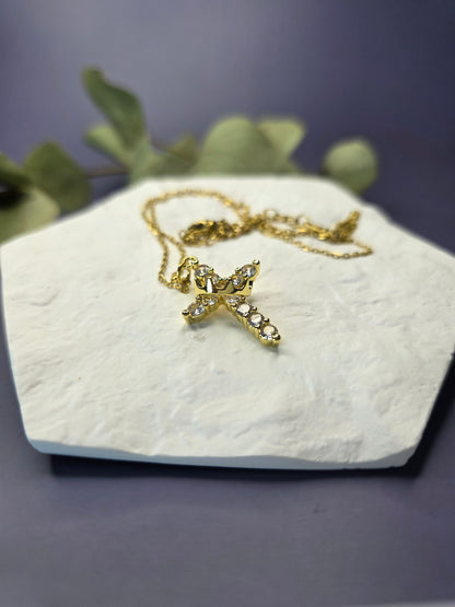 Glimmering Gold Grace necklace draped on a white textured hexagon stone. This 18K gold plated cross jewelry is tarnish-resistant and meaningful for daily wear - My Silver Lining.
