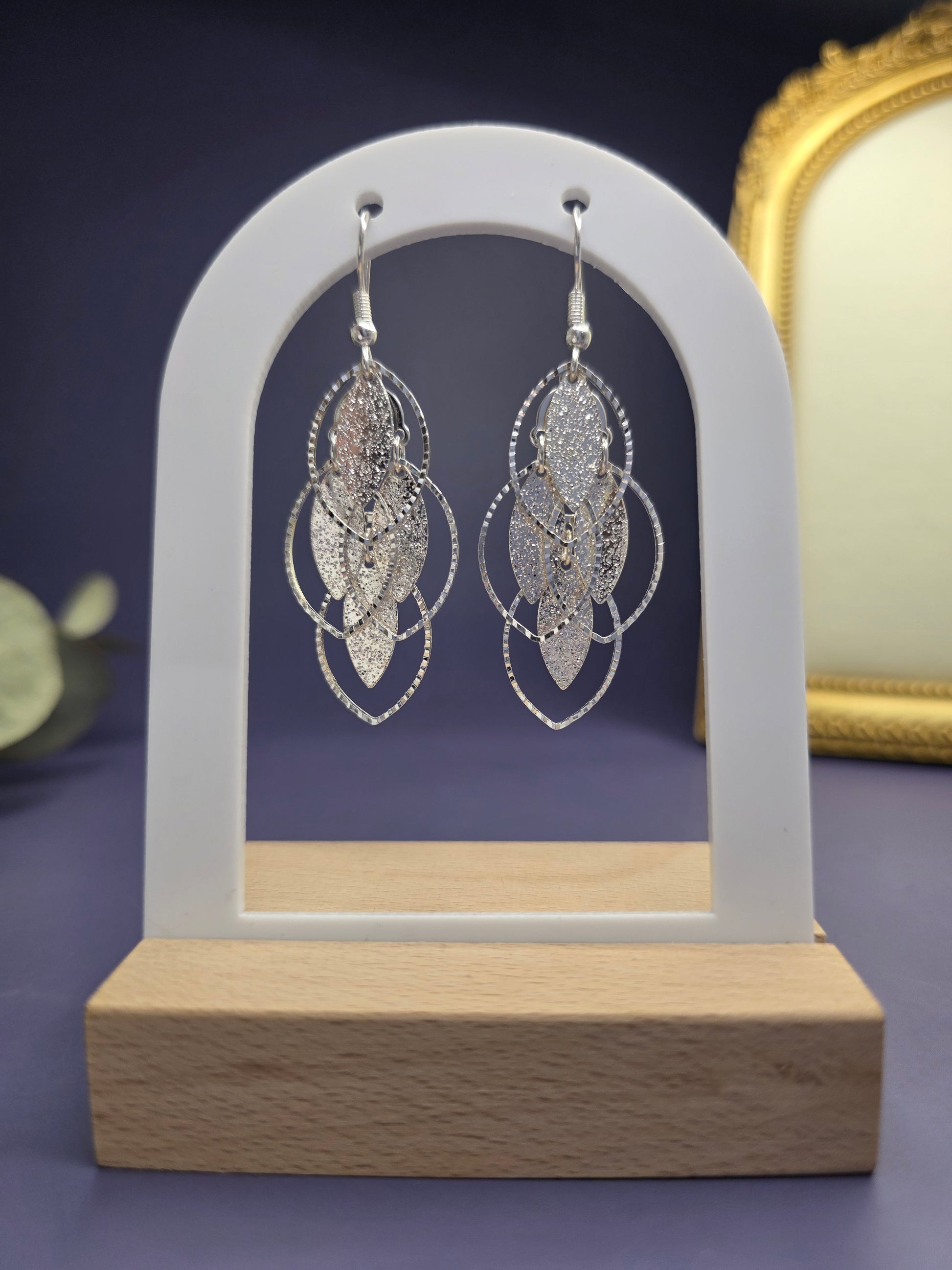 Glitzy Silver Filigree Leaf earrings featured on a white arch jewelry stand. These silver 6cm long tiered leaf earrings offer a sparkling textured finish and a hypoallergenic design for sophisticated wear - My Silver Lining.