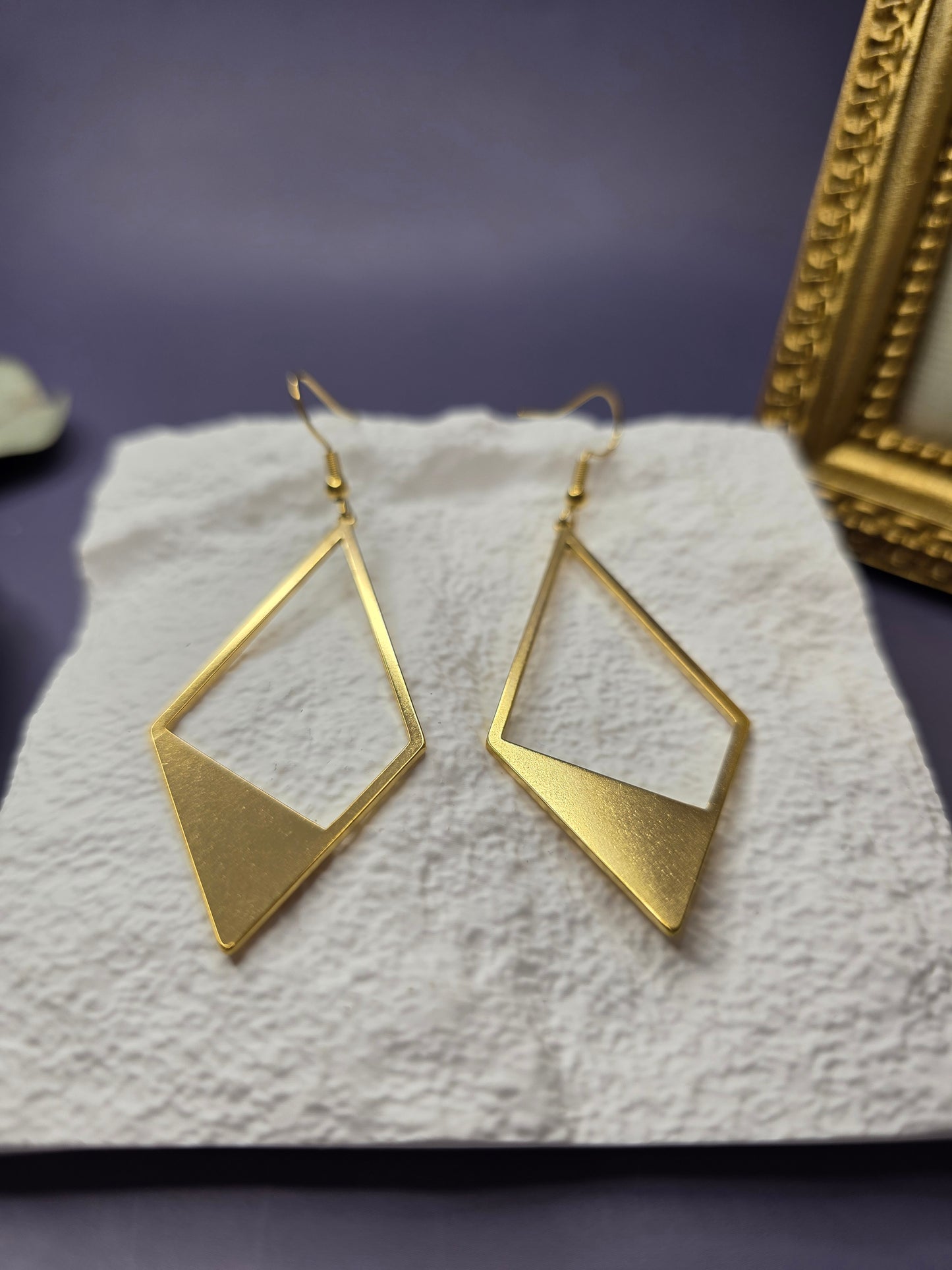 Detail shot of Golden Anchor Drops resting on a white textured stone. High-quality waterproof and tarnish-resistant gold earrings with hypoallergenic medical-grade needles for sensitive ears - My Silver Lining.