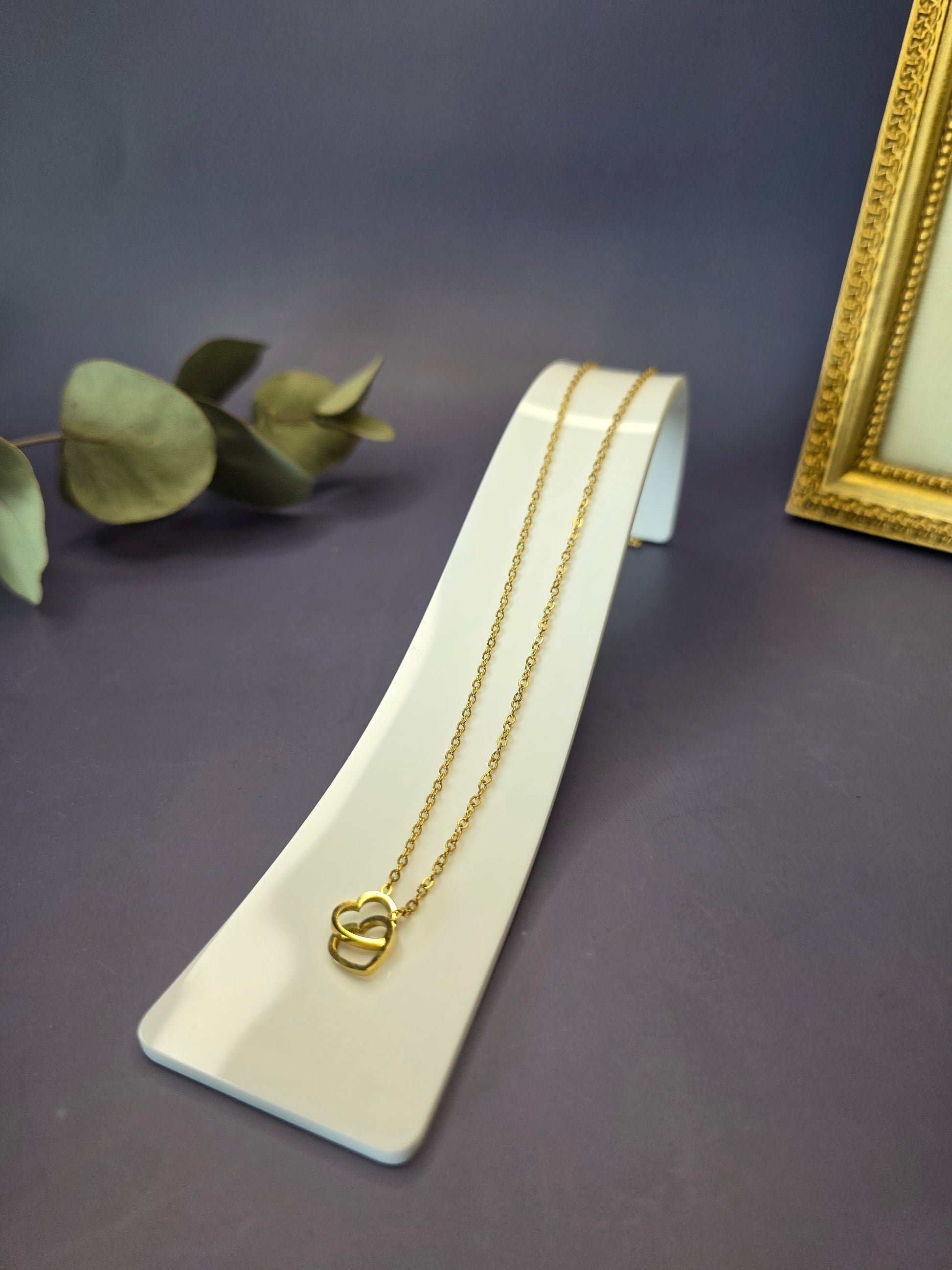 Golden Dual Hearts necklace featuring interlocking heart charms on a sleek white display. This 316 stainless steel gold-plated pendant is waterproof and hypoallergenic - My Silver Lining.
