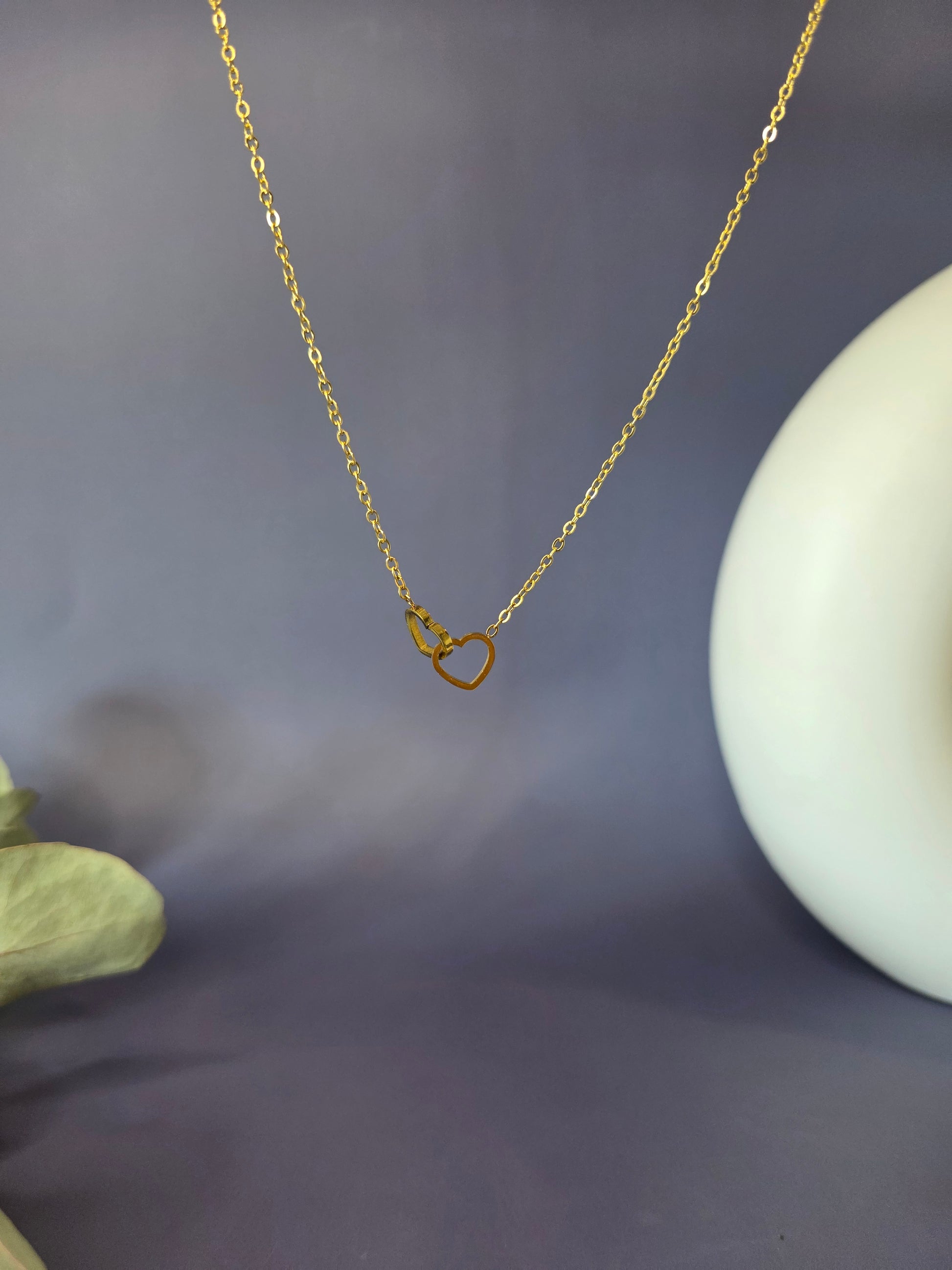Close-up of the Golden Dual Hearts necklace hanging against a soft purple background. Tarnish-resistant KC gold plating over a 316 stainless steel core for lasting everyday brilliance - My Silver Lining.