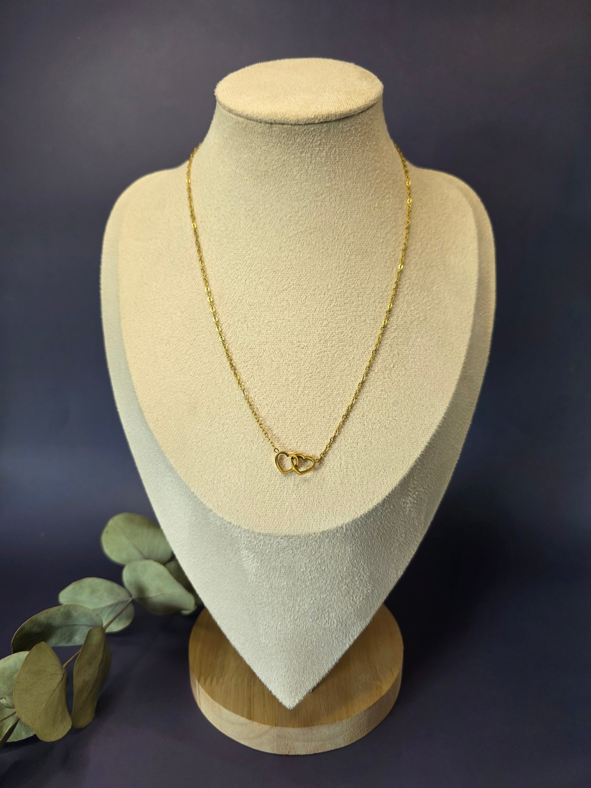 Golden Dual Hearts necklace displayed on a tan jewelry bust. This interlocking heart pendant in 316 stainless steel with KC gold plating offers a waterproof and tarnish-resistant finish for everyday elegance - My Silver Lining.