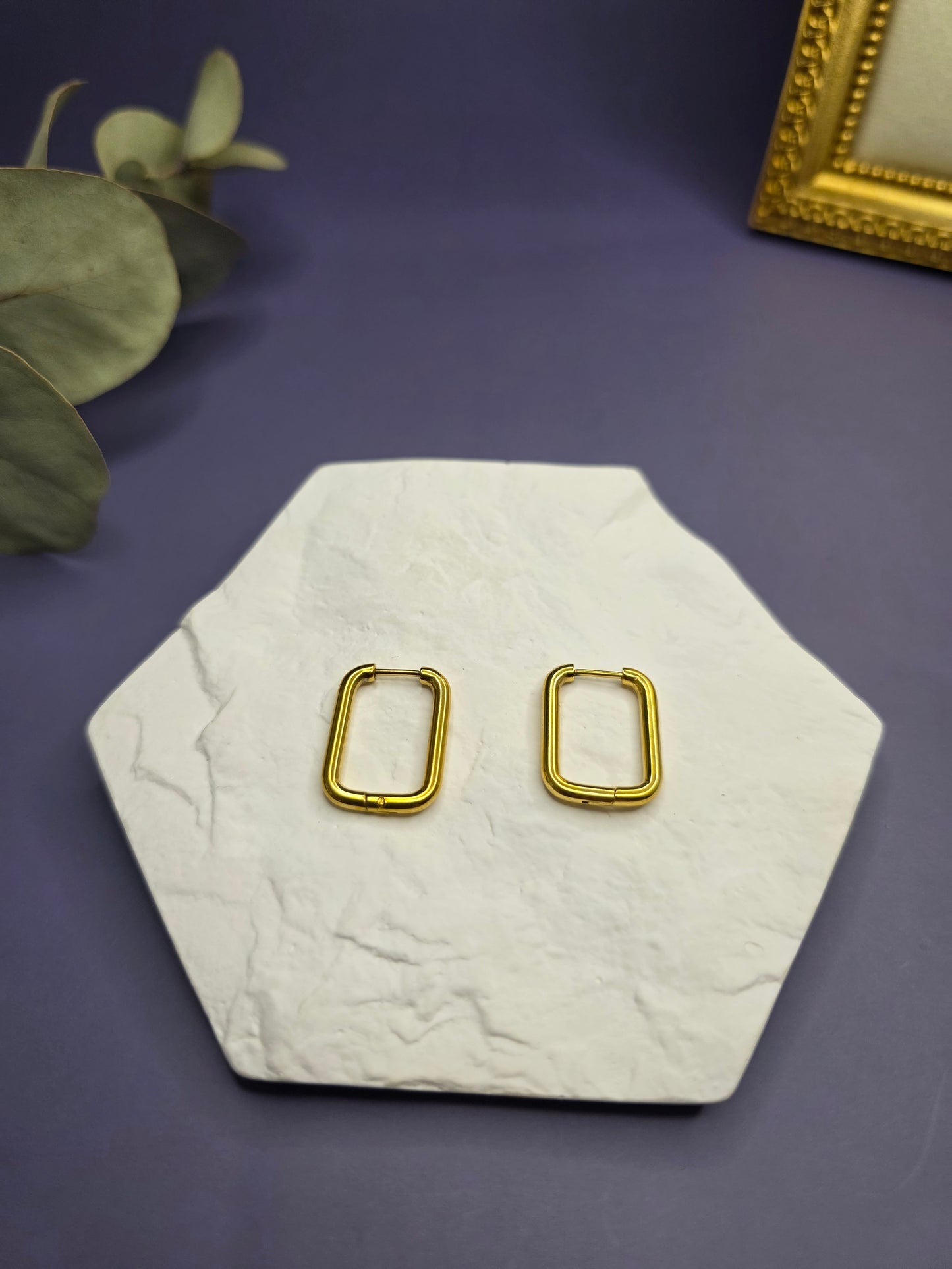 Golden frame hoops displayed on a white textured hexagon stone. These 2cm KC gold plated waterproof sleeper earrings made of 316L stainless steel feature a unique rectangular design - My Silver Lining.
