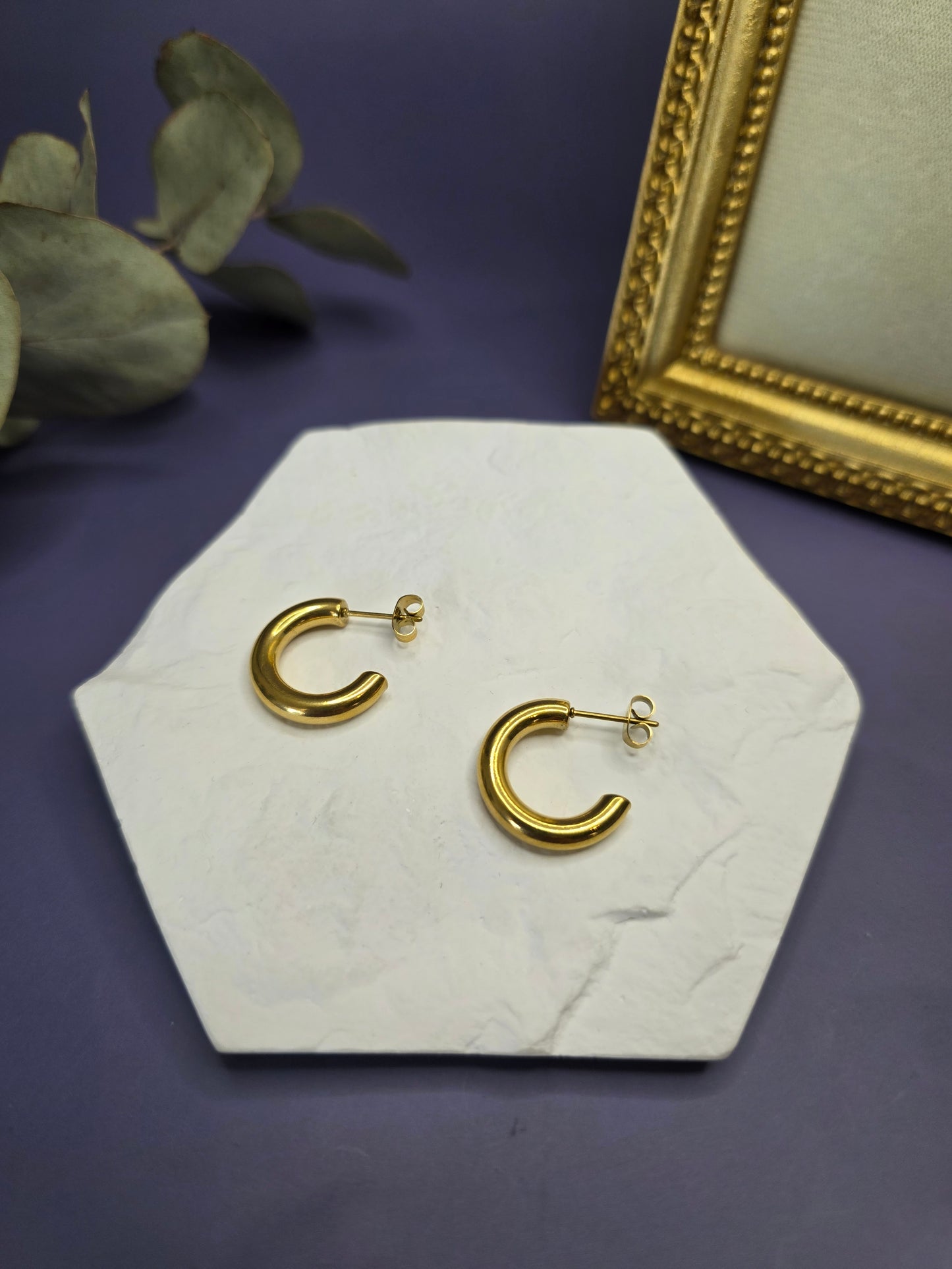 Golden Hollow C-Hoops displayed on a white textured hexagon stone. These 18k gold plated 316 stainless steel earrings are waterproof and hypoallergenic — My Silver Lining.