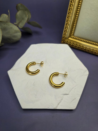 Golden Hollow C-Hoops displayed on a white textured hexagon stone. These 18k gold plated 316 stainless steel earrings are waterproof and hypoallergenic — My Silver Lining.