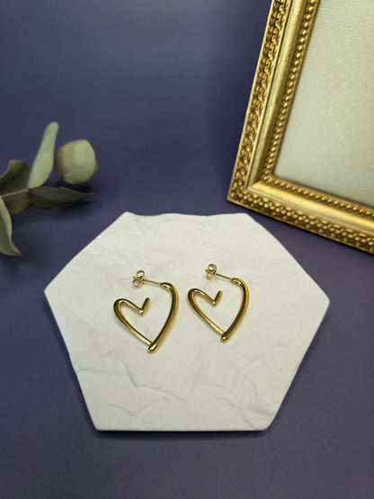 Golden open heart earrings presented in a flat lay on a white textured stone. Crafted from tarnish-resistant 316 stainless steel with a genuine 18k gold finish, these hypoallergenic hoops are designed for durable sophistication - My Silver Lining.