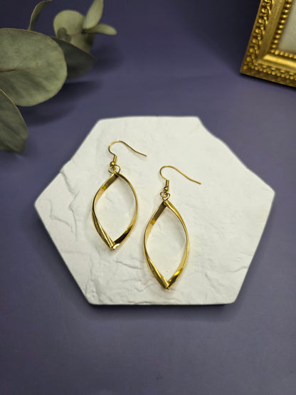 Giolden ribbon earrings displayed on a white textured hexagon stone. These 7cm waterproof 316 stainless steel drop earrings offer a polished, tarnish-resistant twisted design for modern everyday elegance - My Silver Lining.