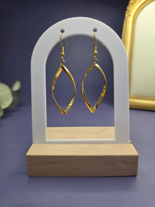 Golden ribbon earrings featured on a white arch jewelry stand. These 316 stainless steel waterproof earrings provide a striking 7cm elongated silhouette and a hypoallergenic finish for sophisticated wear - My Silver Lining.