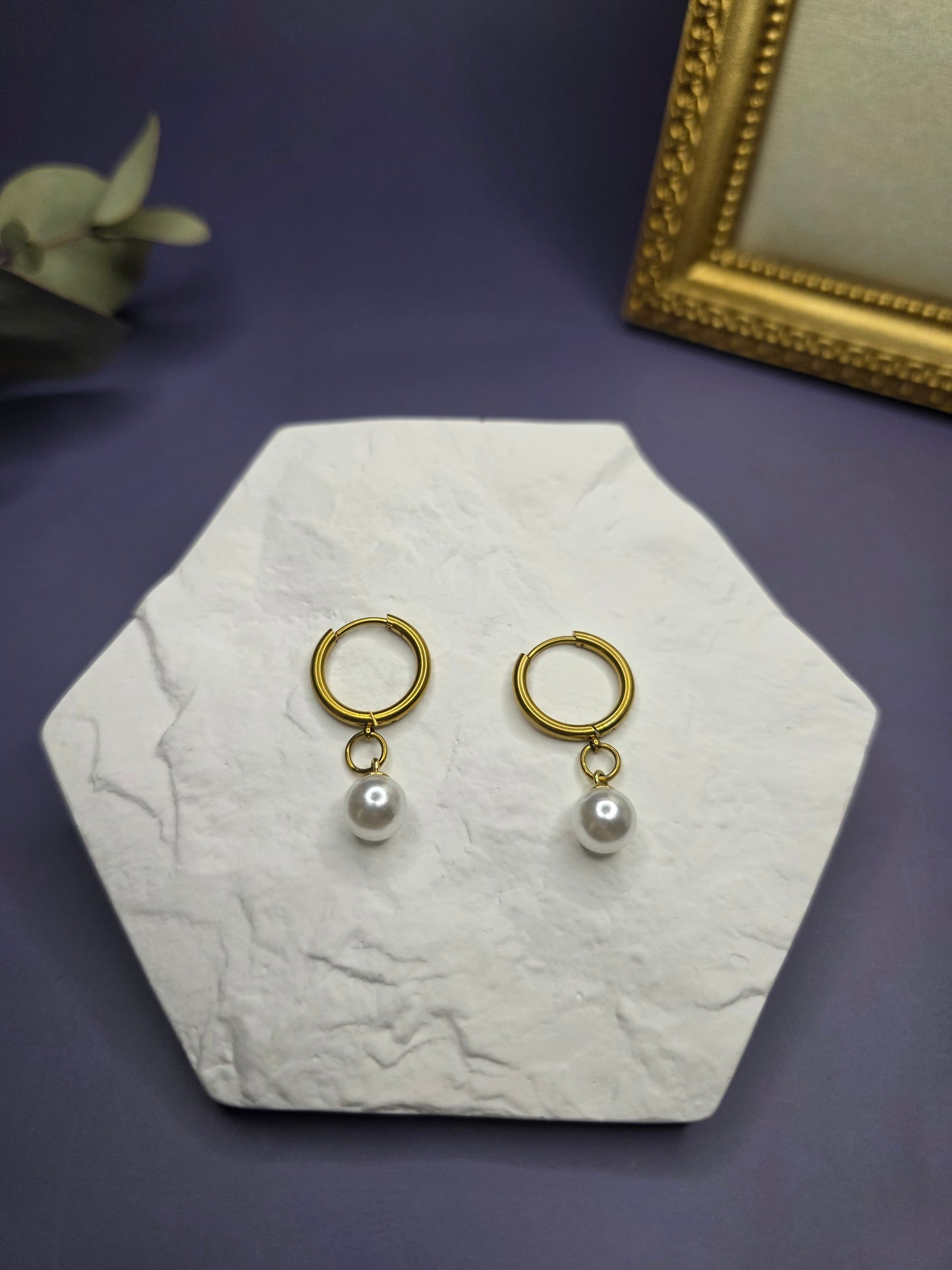 18k gold plated pearl drop earrings showcased on a white textured hexagon stone. These 316 stainless steel waterproof hoops feature a 1cm wide imitation pearl, combining modern durability with classic coastal elegance - My Silver Lining.