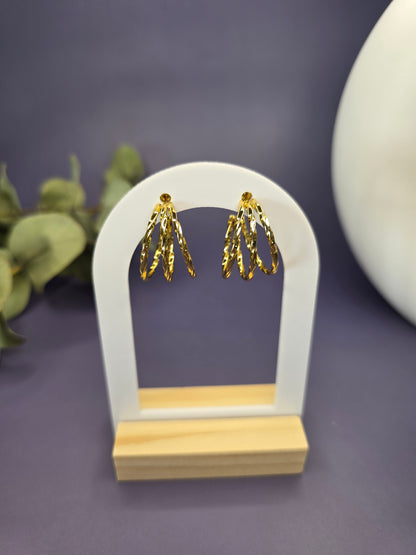 Golden Twist hoops featured on a white arch jewelry stand. These tarnish-resistant 304 stainless steel hoops provide a bold textured silhouette and hypoallergenic finish for comfortable wear - My Silver Lining..