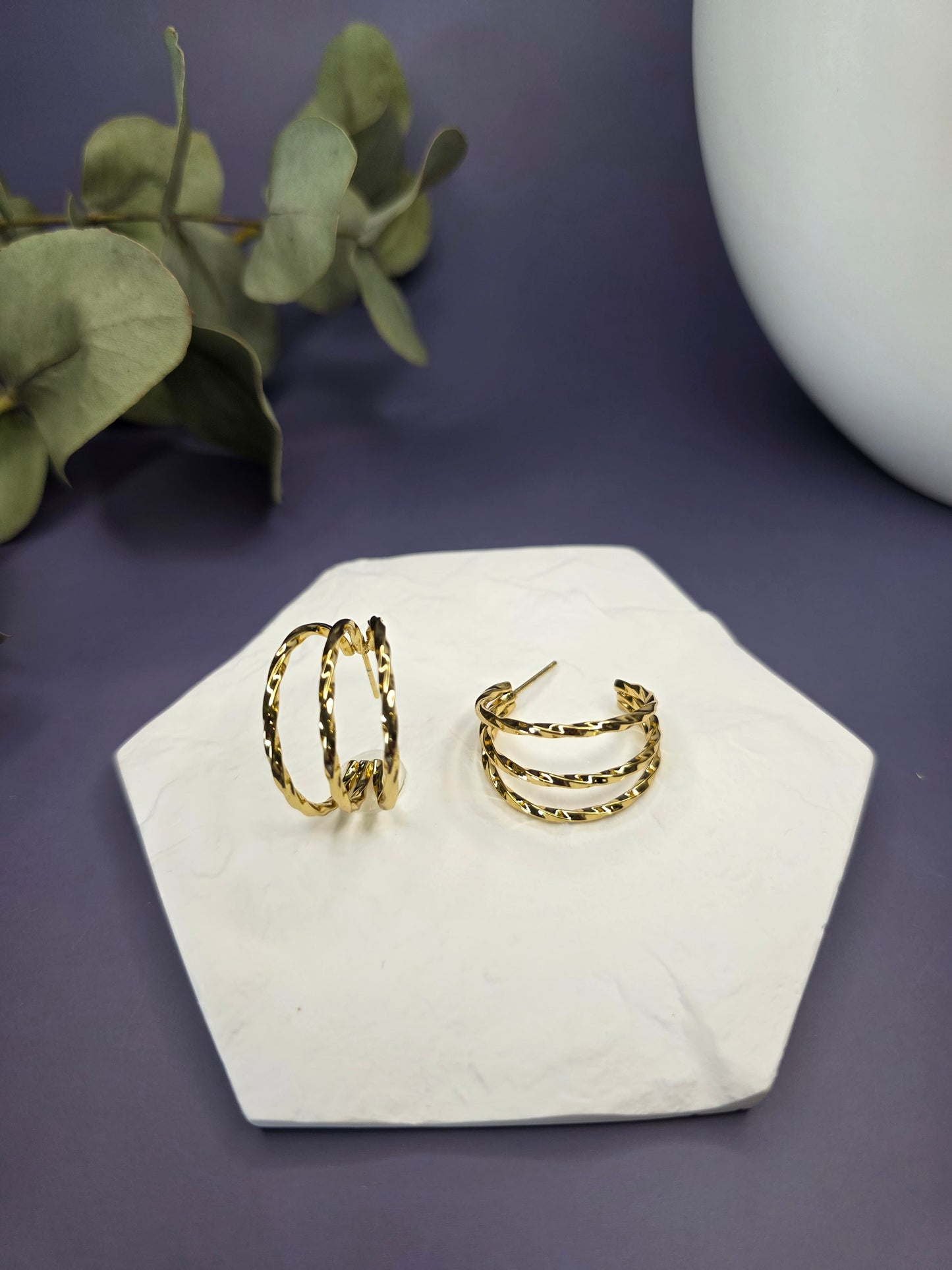 Golden Twist hoops displayed on a white textured hexagon stone. These 2.5cm triple-layered twisted earrings are made of waterproof 304 stainless steel with 316 silver-colored needles - My Silver Lining.