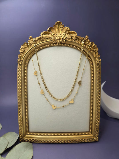 18K gold-plated Heartfelt Journey necklace showcased on a vintage gold frame. This layered stainless steel piece features a bold Figaro chain and dainty heart charms - My Silver Lining.