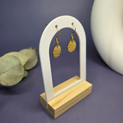 Angled view of the Honey Gold Hammered Drops, showcasing the depth of the textured finish and the secure hook design on a white arch display stand.