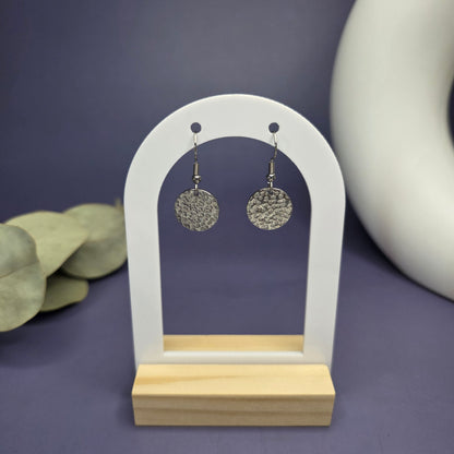 Frontal view of the Silver Sands Hammered Drops on a white and wood arch stand, showcasing the textured 316 stainless steel finish — My Silver Lining.
