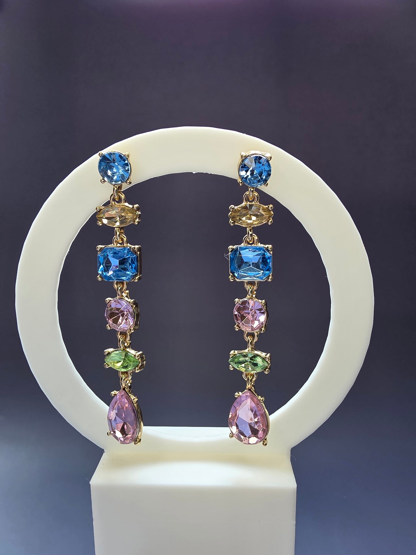 Jeweled Cascade drop earrings featured on a white arch jewelry stand. These 18K gold plated statement earrings provide a colorful stone-encrusted silhouette and long vertical drop - My Silver Lining.