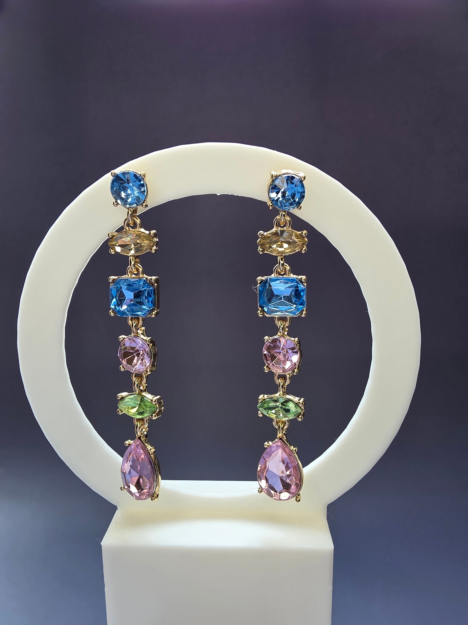 Jeweled Cascade drop earrings featured on a white arch jewelry stand. These 18K gold plated statement earrings provide a colorful stone-encrusted silhouette and long vertical drop - My Silver Lining.