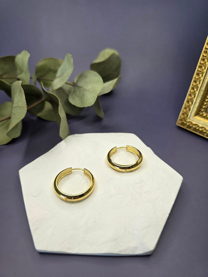 Line of Luxe hoops displayed on a white textured hexagon stone. These 2.5cm 18K gold plated waterproof earrings made of 304 stainless steel feature a wide huggie design - My Silver Lining.