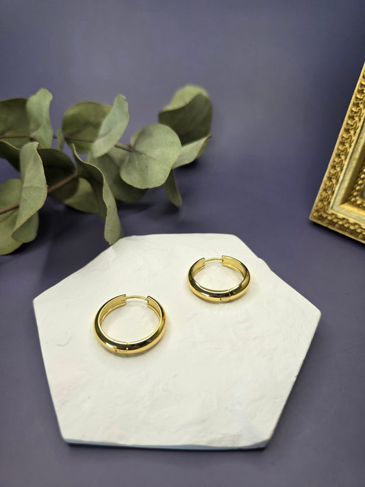 Line of Luxe hoops displayed on a white textured hexagon stone. These 2.5cm 18K gold plated waterproof earrings made of 304 stainless steel feature a wide huggie design - My Silver Lining.