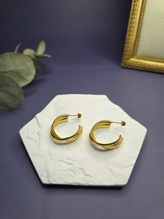Metric Tides hoops displayed on a white textured hexagon stone. These 2.5cm KC gold plated waterproof sleeper earrings made of 316 stainless steel feature a unique triple-band design - My Silver Lining.