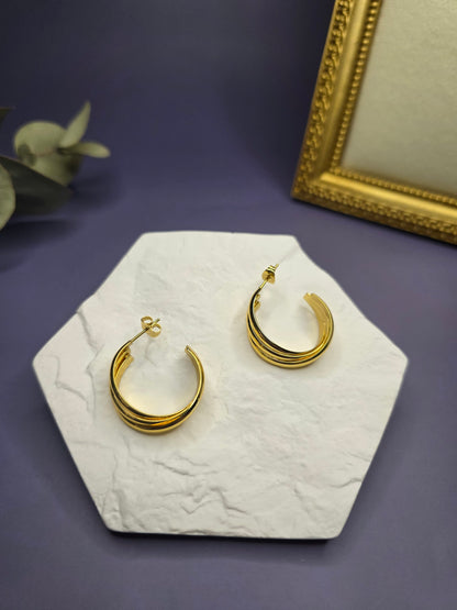 Metric Tides hoops displayed on a white textured hexagon stone. These 2.5cm KC gold plated waterproof sleeper earrings made of 316 stainless steel feature a unique triple-band design - My Silver Lining.2
