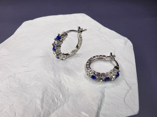Midnight Starlight huggie hoops displayed on a white textured hexagon stone. These 1.82cm S925 sterling silver earrings feature alternating blue and white stones for modern everyday elegance - My Silver Lining.