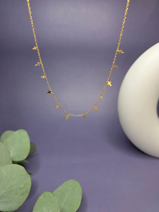 Close-up of the Mini Cross Charm Necklace in a floating composition against a purple background. This waterproof 18k gold plated jewelry features 0.4cm and 0.6cm cross charms, offering a refined and contemporary aesthetic.
