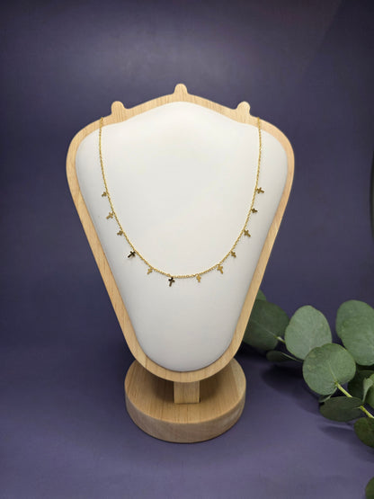 18k Gold plated mini cross charm necklace presented on a white shield-shaped jewelry stand. This 304 stainless steel waterproof necklace features multiple delicate crosses for a modern, sophisticated look.