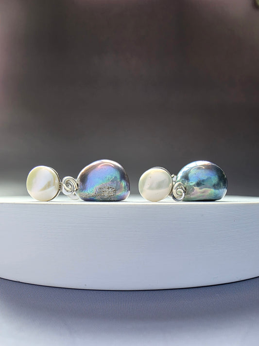 The Black Moon Drops. Elegant earrings featuring a white freshwater pearl stud and a large, iridescent black baroque pearl drop. Secured with a Stainless Steel post. Note: As genuine freshwater pearls, size and shape vary. The earrings measure approximately 2.2 cm long