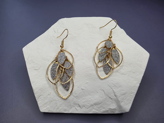 The Glitzy Filigree Leaf Drop Earrings. Long statement earrings, 6 cm in length, featuring a multi-tiered leaf design with textured and open filigree sections, finished in 18K Gold Plating. The ear needle is stainless steel