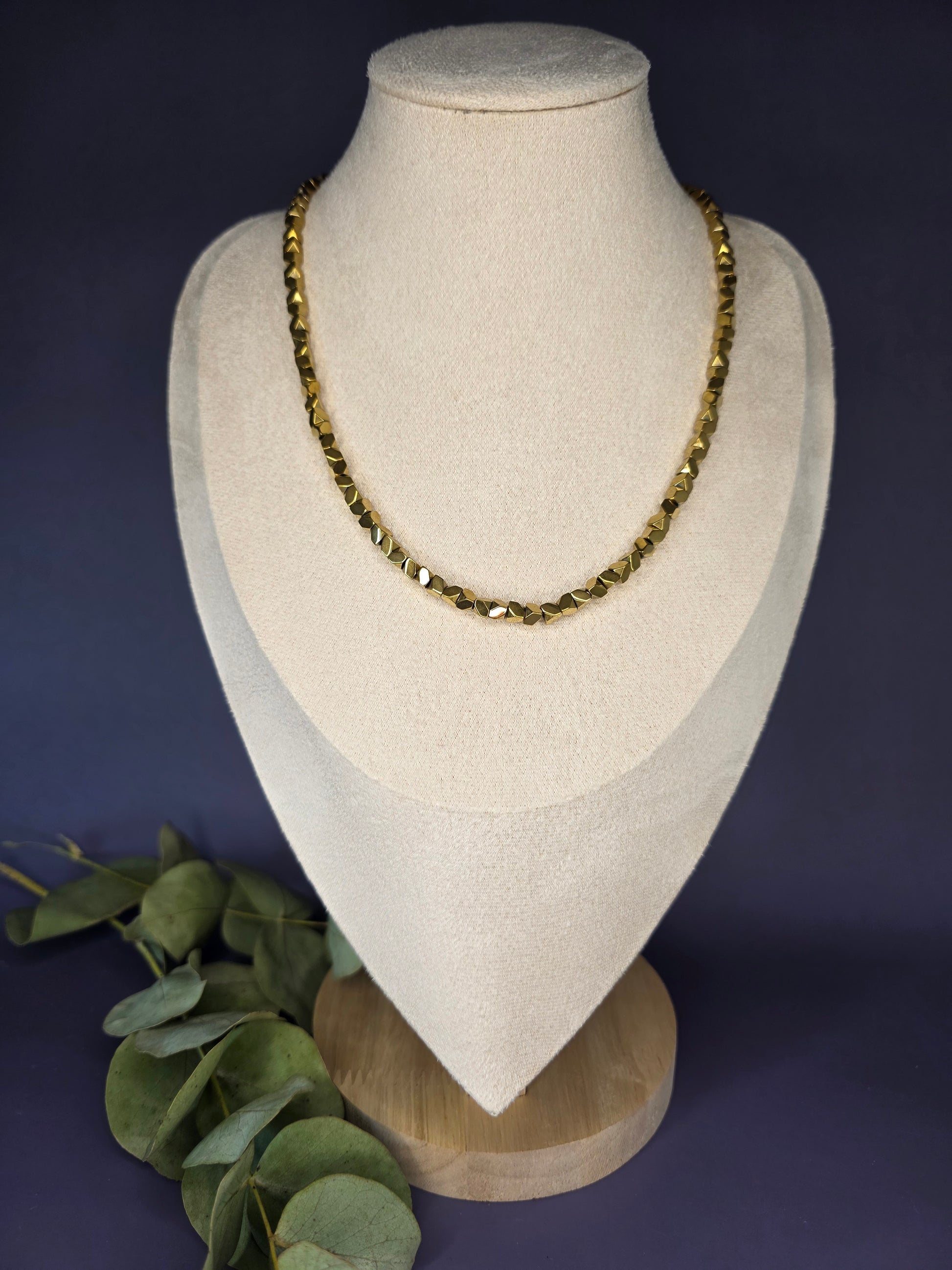 The Solaris Chain necklace, made of small, gold-toned faceted beads, displayed on a beige jewelry bust. This stainless steel chain is 40 cm long with a 5 cm extender, perfect for a minimalist and boho style.