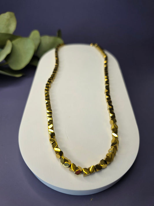 The Solaris Chain necklace, made of small, gold-toned faceted beads, displayed on a beige jewelry bust. This stainless steel chain is $40 \text{ cm}$ long with a $5 \text{ cm}$ extender, perfect for a minimalist and boho style.