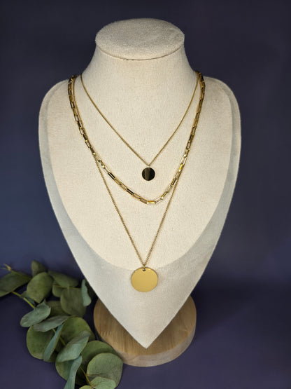 The Golden Harmony Trio, an stainless steel three-layer necklace set, displayed on a beige jewelry bust. The single-piece design includes a small disc, a rectangular link chain, and a large, reflective disc pendant, showcasing a perfectly stacked look.