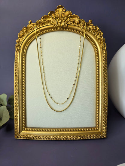 The Golden Line Harmony necklace, a double-piece, double-layered silver-toned necklace featuring a smooth flat chain and a fine beaded satellite chain