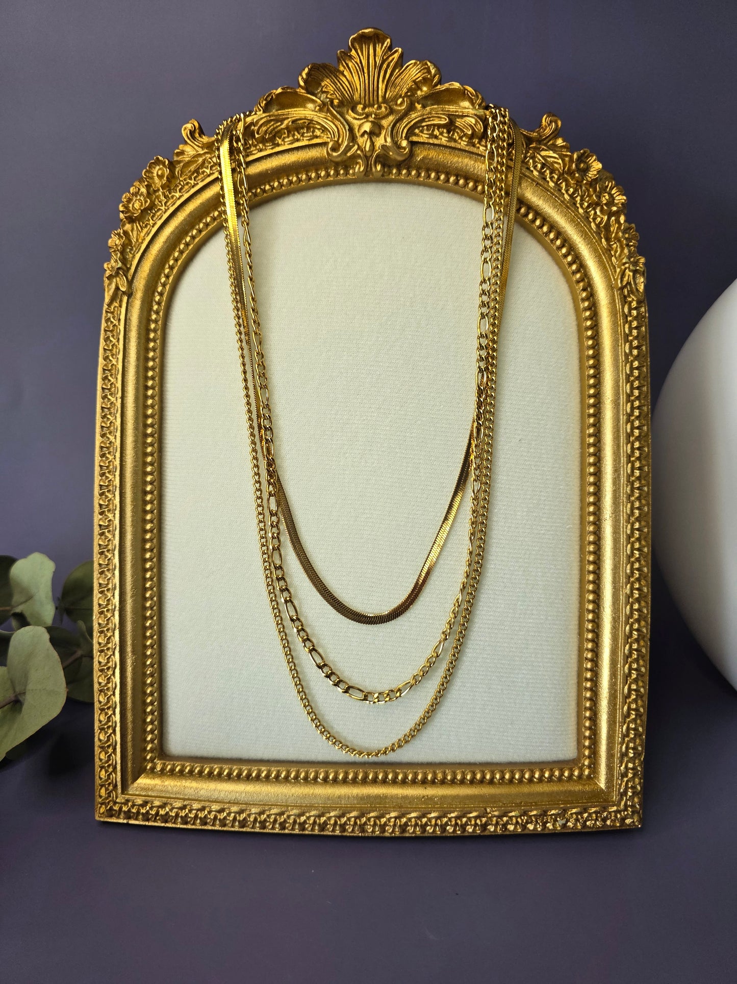 The Golden Texture Trio, a set of three separate gold-plated stainless steel necklaces for layering. The set includes a smooth herringbone chain, a classic figaro chain, and a fine twisted chain.