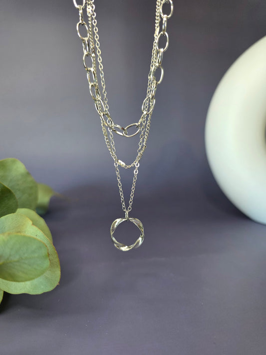 The Silver Line Loop necklace, a single-piece, three-layer necklace set in 925 silver-plated copper. The layers include a chunky oval link chain, a fine chain, and a twisted ring pendant.