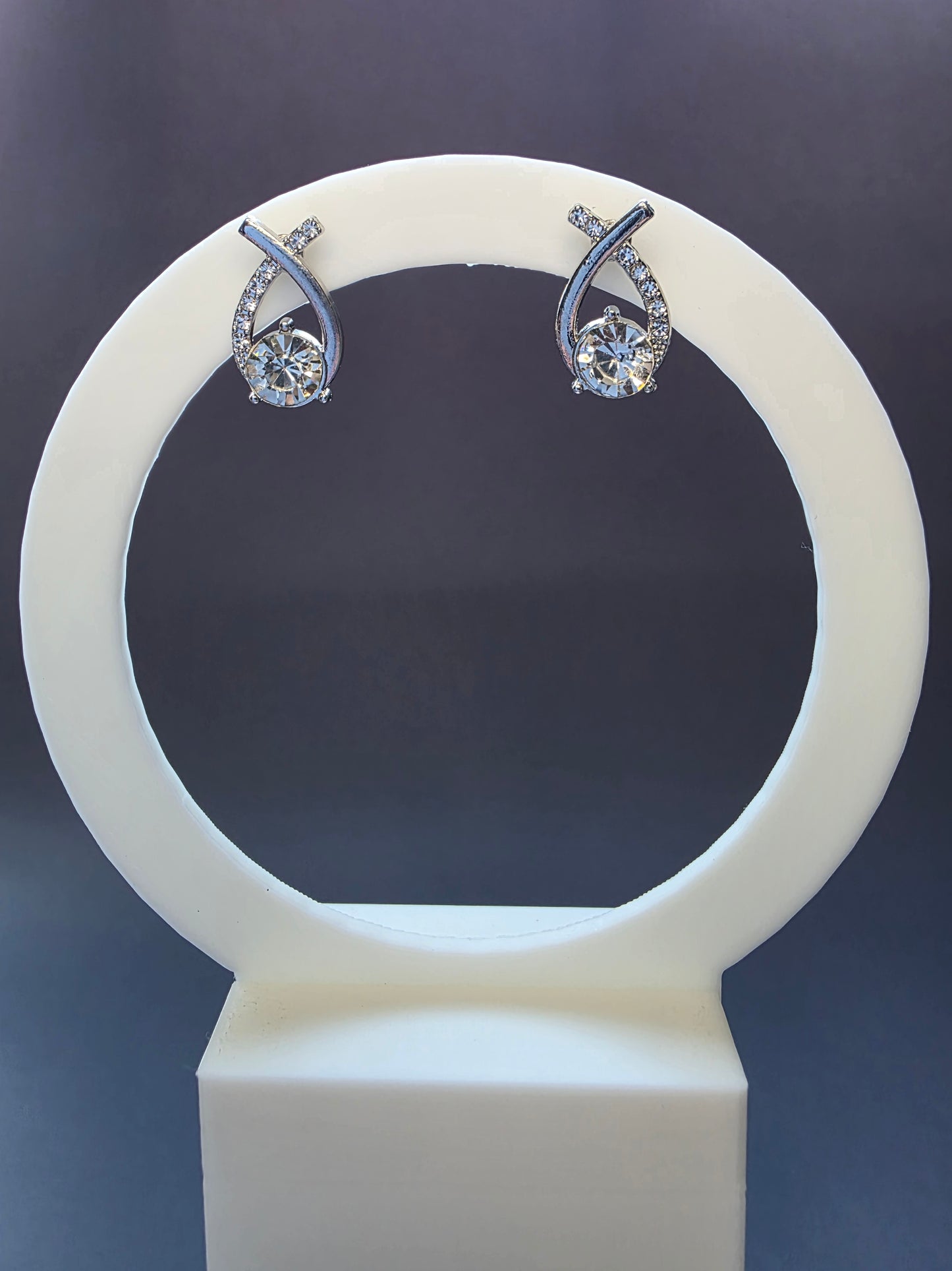 The Nova Orbit Stud Earrings. Silver-toned asymmetrical earrings measuring 1.8 cm long, featuring a brilliant central rhinestone framed by a curved band of accent rhinestones. The ear needle is stainless steel for comfort.
