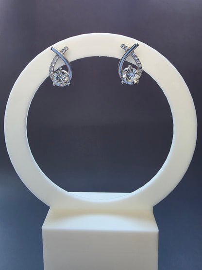 The Nova Orbit Stud Earrings. Silver-toned asymmetrical earrings measuring 1.8 cm long, featuring a brilliant central rhinestone framed by a curved band of accent rhinestones. The ear needle is stainless steel for comfort.