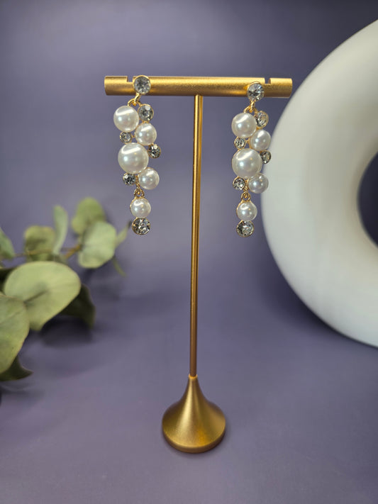 The Pearl Cluster Drops. Gold-plated statement earrings, 5 cm long, featuring a cascading cluster design of imitation pearls and brilliant rhinestones. Secured with a Stainless Steel post