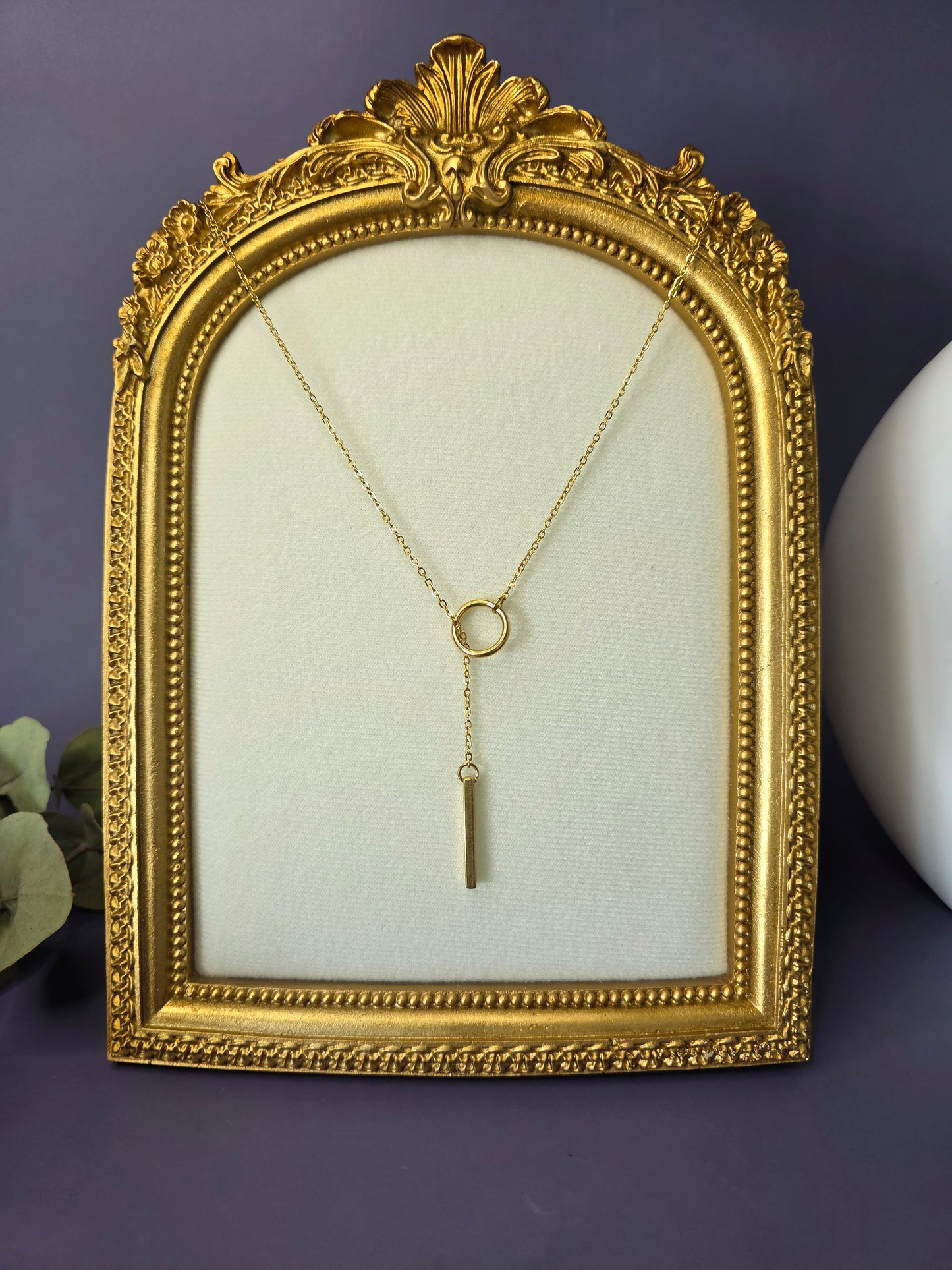 The Sleek Gold Y-Necklace Choker, a gold-plated stainless steel lariat necklace featuring a fine chain, a small circular component, and a polished vertical bar drop pendant